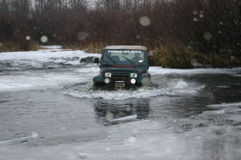 2003 Jeep TJ - A green Jeep TJ navigates through icy water, with a "KODIAK OFF-ROAD" sticker visible on its windshield.