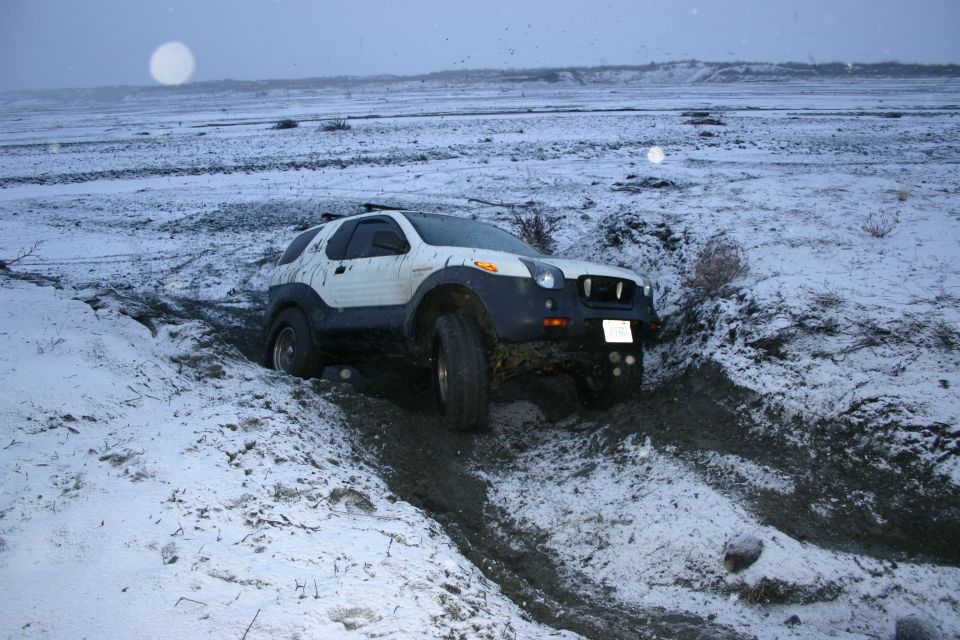 White and black SUV stuck in a muddy ditch with snow on the ground