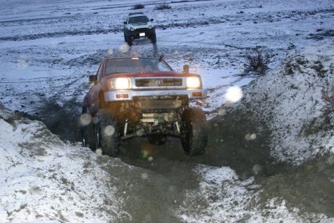 2003 Jeep TJ - A red Toyota pickup truck navigates a challenging snowy and muddy terrain with another vehicle following behind.