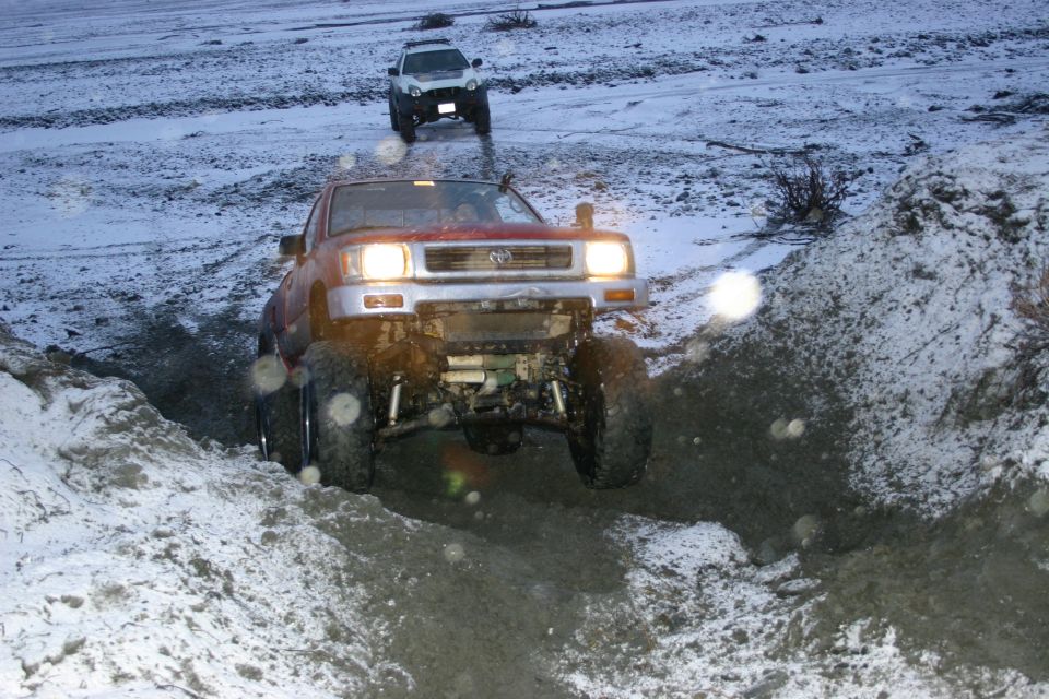 Red Toyota pickup truck with lifted suspension driving on a snowy, muddy trail