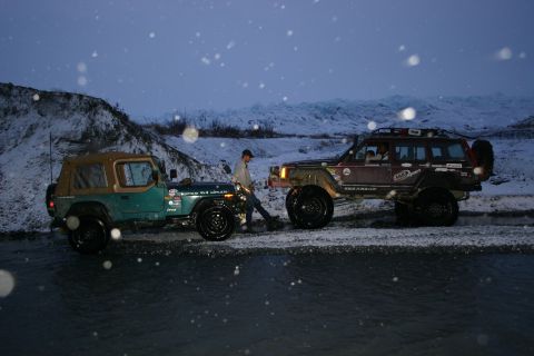 2003 Jeep TJ - Two Jeep SUVs, a green CJ-7 and a brown Cherokee XJ, navigate a snowy, watery terrain under a twilight sky.