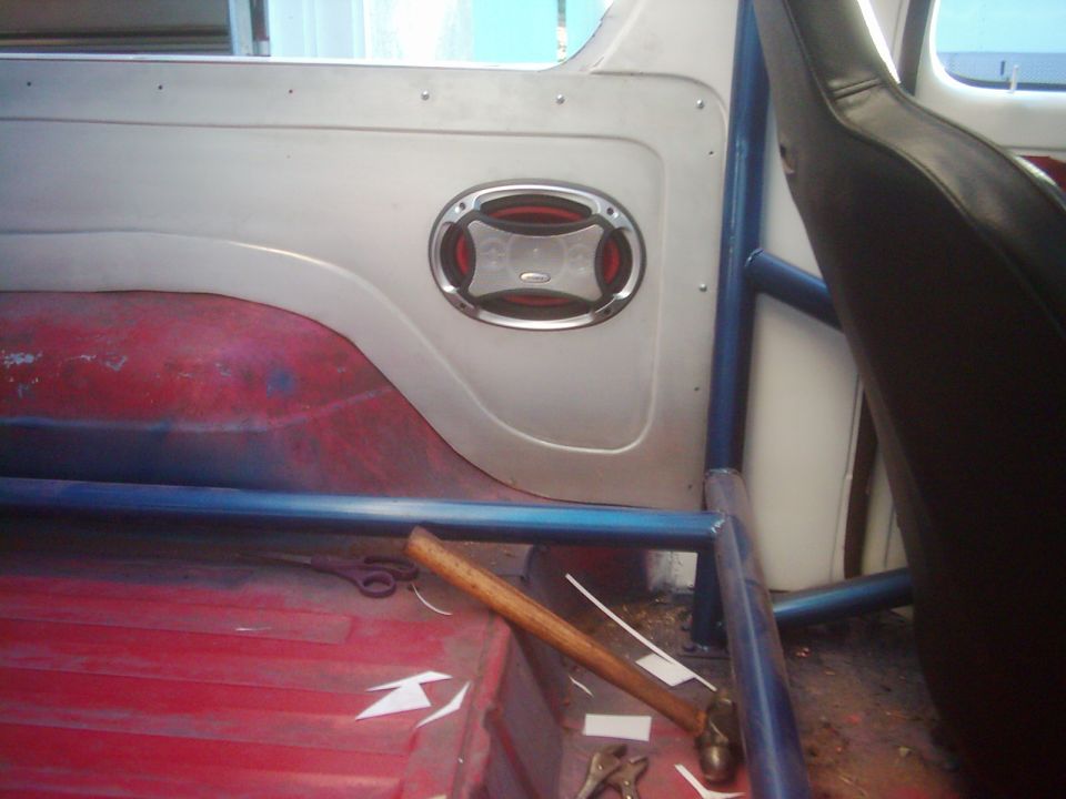 Interior shot of a vehicle showing a blue roll cage, a speaker, and a seat. A hammer and scissors are on the floor