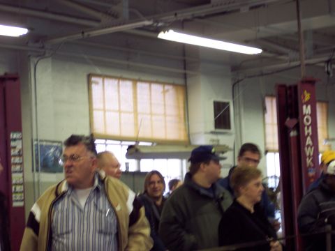 1991 Ford LTD Crown Victoria - A group of people stand in a garage setting, with visible lift equipment and overhead lights.