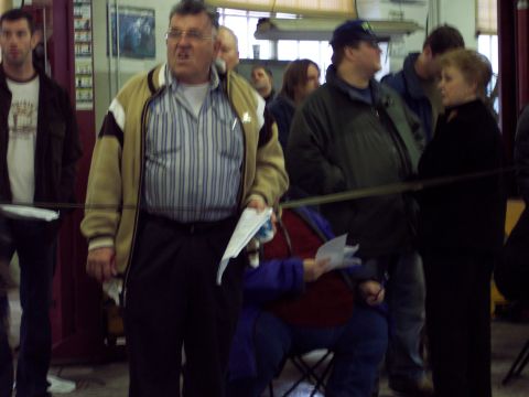 1991 Ford LTD Crown Victoria - A group of people are gathered indoors, with one man in the foreground holding papers.