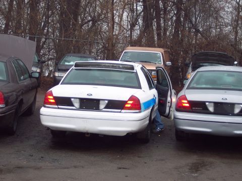 1991 Ford LTD Crown Victoria - Multiple police cars are parked in an outdoor lot. One white car has its driver's side door open.