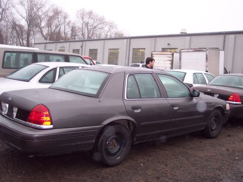1991 Ford LTD Crown Victoria - A dark gray sedan is parked in a lot with other vehicles and buildings in the background.