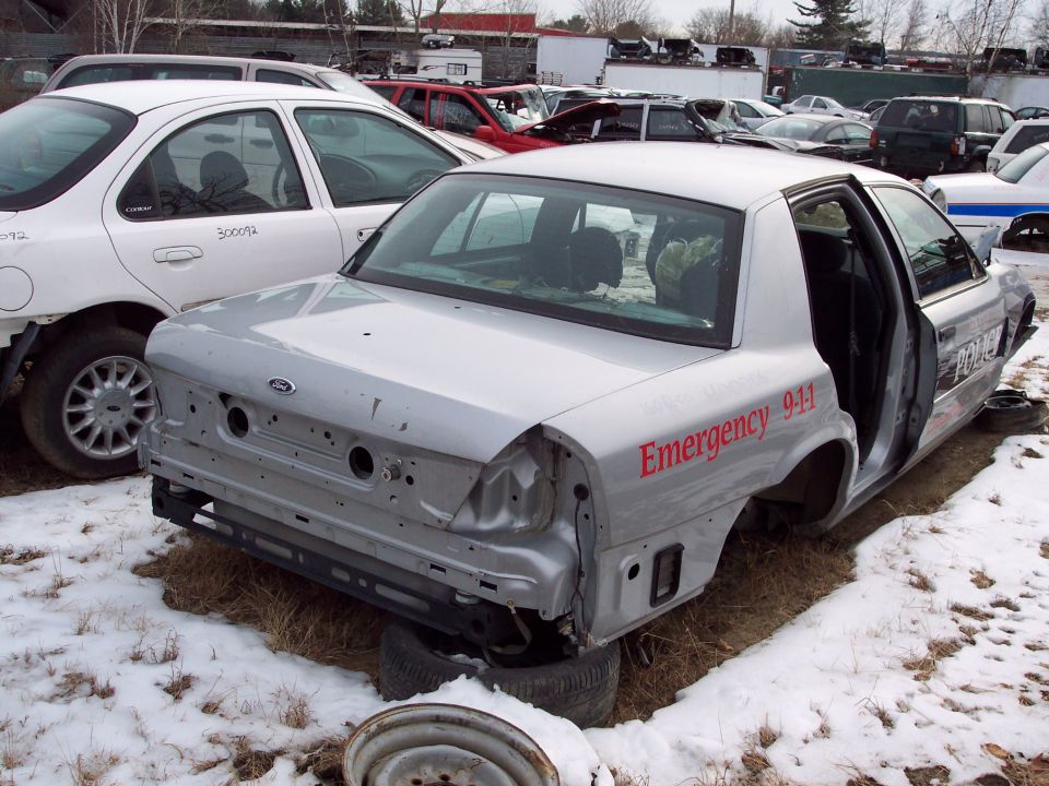 Silver Ford Crown Victoria with 'Emergency 911' and 'POLICE' text, missing bumpers and doors