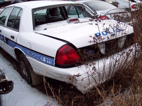 1991 Ford LTD Crown Victoria - Rear view of a damaged white police car parked in an outdoor lot with snow on the ground.