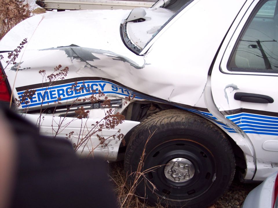 damaged white police car with blue stripe and 'EMERGENCY 911' text, showing significant rear quarter panel damage