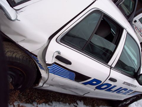 1991 Ford LTD Crown Victoria - A damaged white police car with 'PETERBOROUGH POLICE' text is seen from the side, with another vehicle visible in the background.