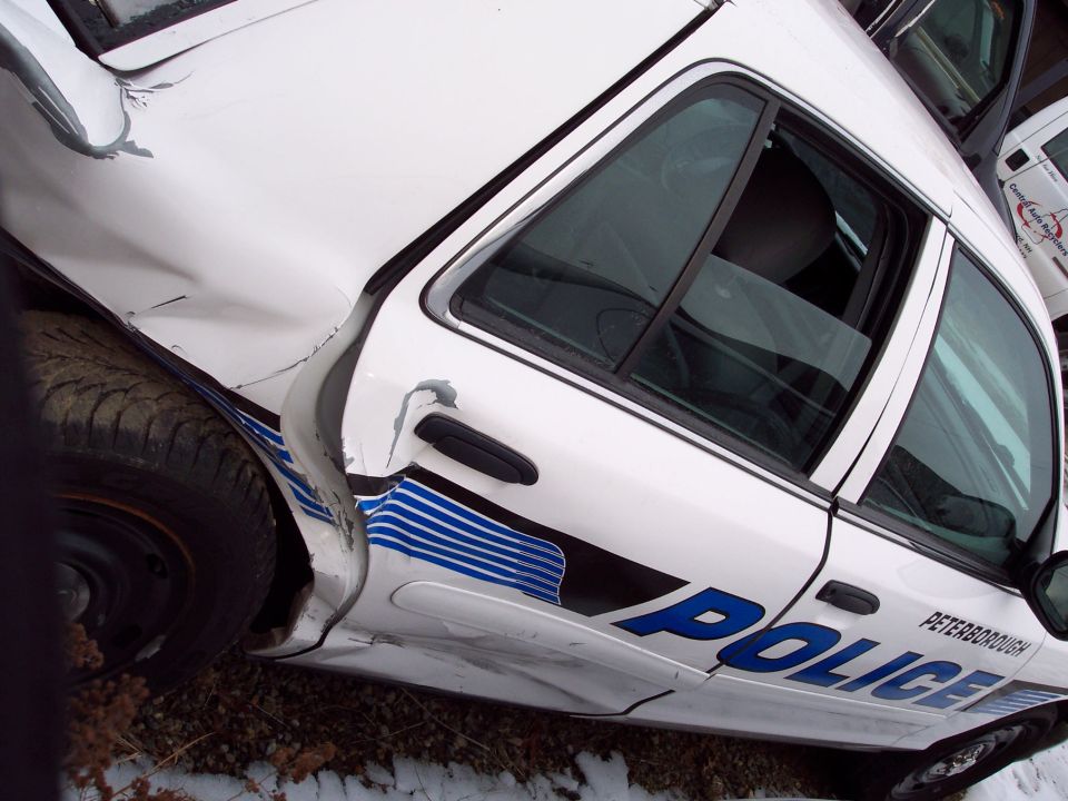 White police car with blue stripes and 'POLICE' text, showing significant rear quarter panel damage