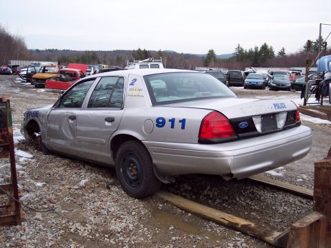 1991 Ford LTD Crown Victoria - Junkyard police car with '911' and 'POLICE' markings, missing front wheels.