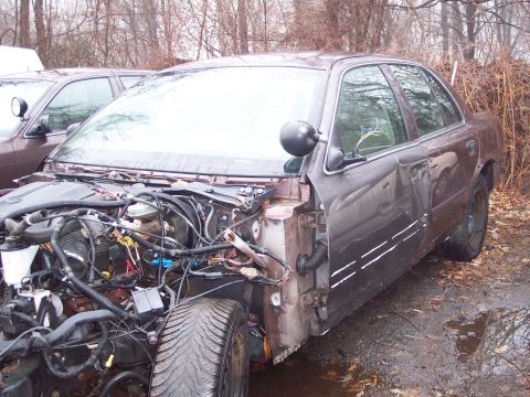 1991 Ford LTD Crown Victoria - A damaged 1991 Ford Crown Victoria LTD sits in a junkyard with its front end dismantled.