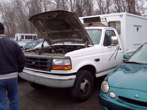 1991 Ford LTD Crown Victoria - White truck with hood open, parked next to a teal car. A person stands to the left of the truck.