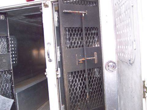 1991 Ford LTD Crown Victoria - The interior of a van or truck shows metal shelving and a reinforced cage door with a locking mechanism.