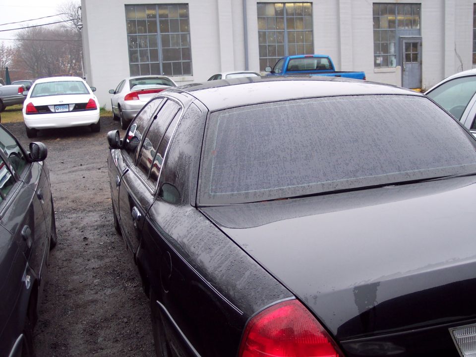 Black Ford Crown Victoria parked next to another car. White Ford Crown Victoria in background
