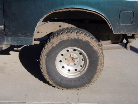 1995 Ford Bronco - The rear wheel well of a dark green Ford Bronco shows significant rust and mud on the tire.