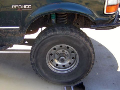 1995 Ford Bronco - Close-up of the front wheel and fender of a dark green Ford Bronco, revealing its suspension components.