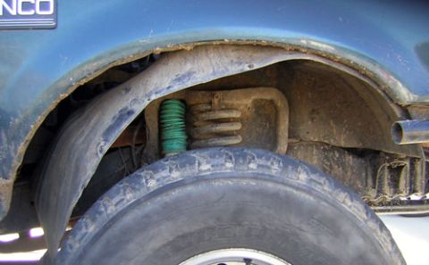 1995 Ford Bronco - Close-up of the rear wheel well of a blue 1995 Ford Bronco, showing suspension components and signs of wear.