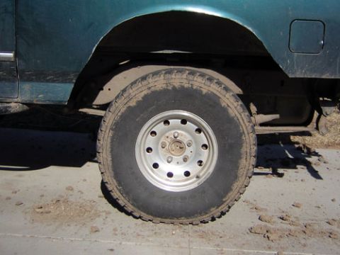 1995 Ford Bronco - Close-up of the rear wheel and fender of a teal truck, showing an aggressive all-terrain tire on a silver slotted steel wheel with an eight…