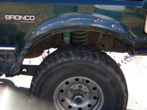 1995 Ford Bronco - Close-up of the front wheel well on a dark green Ford Bronco XLT, showing the coil spring and shock in the lifted suspension with the inner…