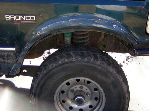 Front wheel well of green Ford Bronco XLT showing coil spring, shock and mud tire