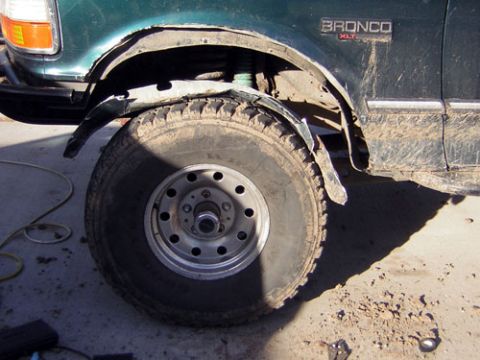1995 Ford Bronco - The side view of a green 1995 Ford Bronco XLT shows damage to the fender and mud on the body.