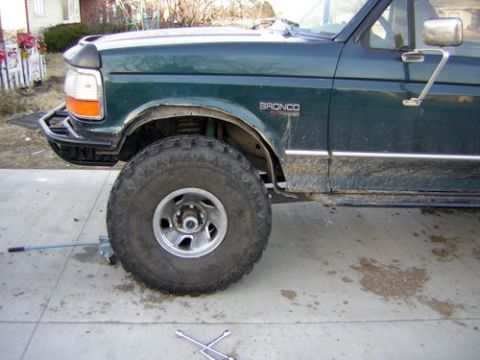 1995 Ford Bronco - Close side view of the front fender and wheel of a dark green Ford Bronco, with an oversize mud-terrain tire on a five-spoke alloy wheel fi…