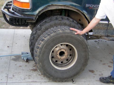 1995 Ford Bronco - A dirty mud-terrain tire on a white eight-lug wagon wheel leans against the front fender of a green Bronco XLT lifted on a floor jack, with…