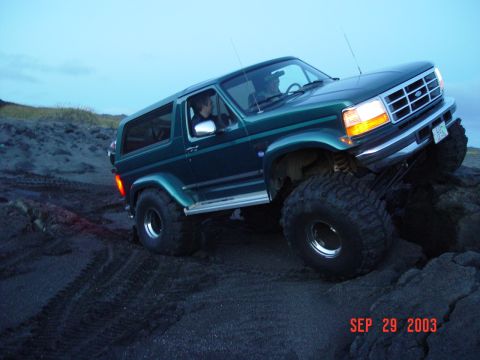 1996 Ford Bronco - 1996 Ford Bronco navigates a rocky, sandy terrain under a twilight sky.