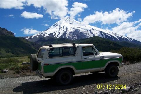 1979 Ford Bronco - A two-tone green and white 1979 Ford Bronco is parked on a dirt road with a snow-covered mountain dominating the background.