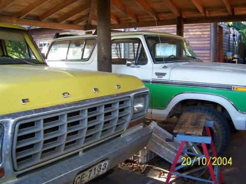 1979 Ford Bronco - Two classic Ford trucks are parked under a covered area, one yellow and one white with green trim.