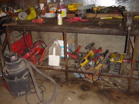 1992 Ford Bronco - A workbench is covered in tools and equipment, including grinders, a shop vac, and a battery.