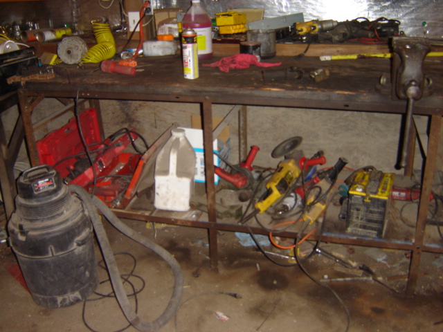 Workbench cluttered with power tools, shop vac, and various supplies