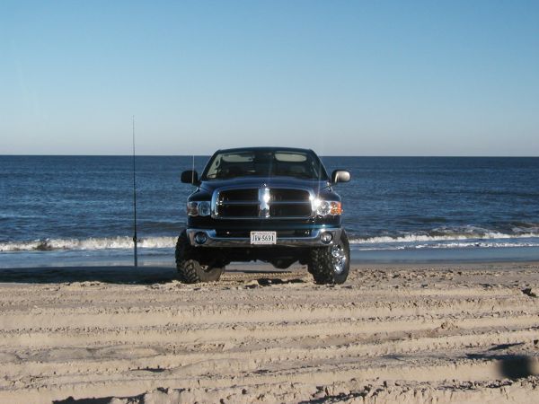 Dark blue Dodge Ram pickup parked on the beach at the waterline, front view