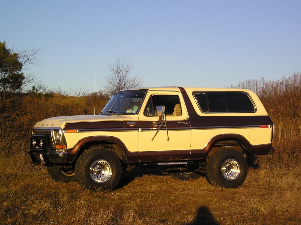 Tan and brown lifted Ford Bronco SUV in side view parked in a field