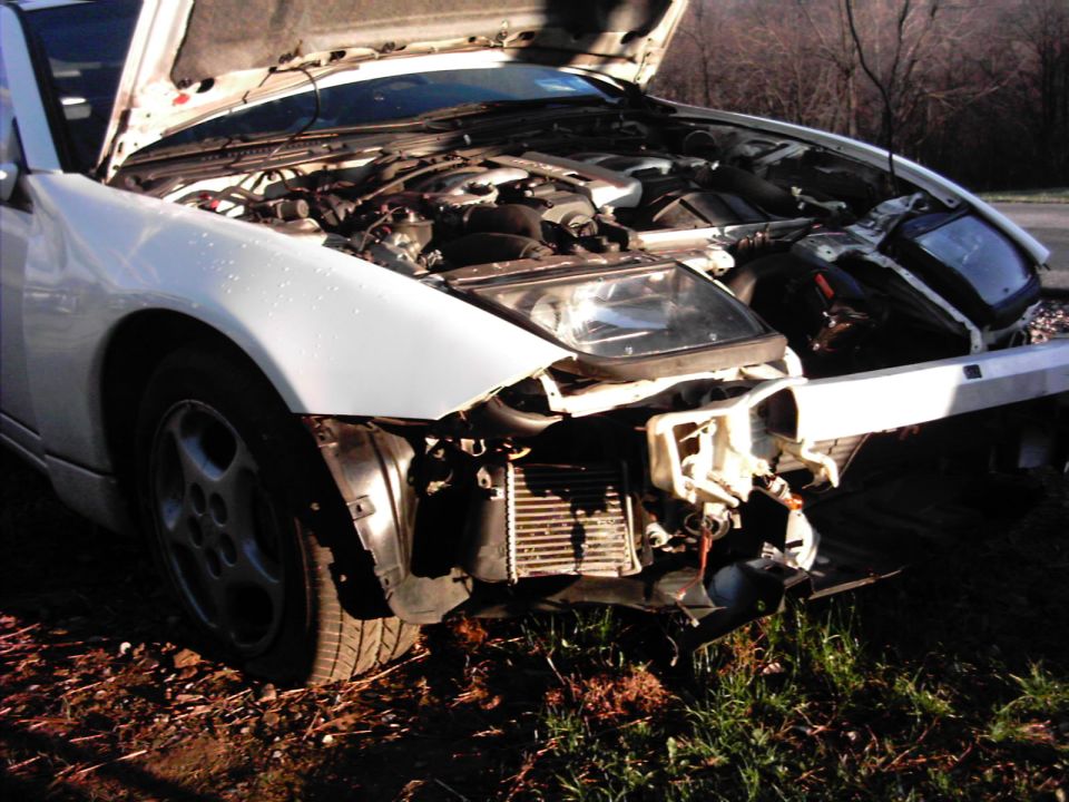 White sports car with hood up and front clip stripped after a front-end collision