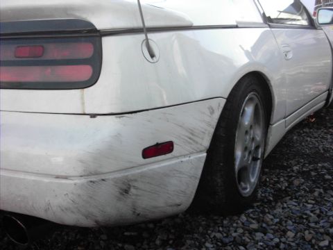1988 Ford LTD Crown Victoria - Close-up of the left rear quarter and bumper of a white Nissan 300ZX (Z32) parked on gravel, showing black scuff marks and rub damage acros…