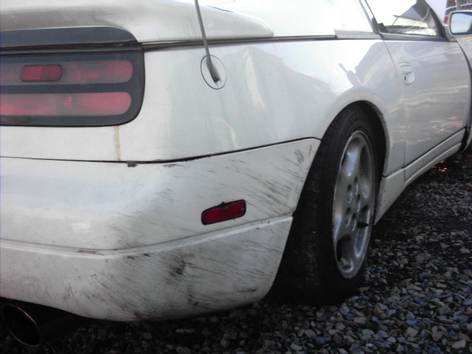 Scuffed rear bumper and quarter panel of a white Nissan 300ZX on gravel