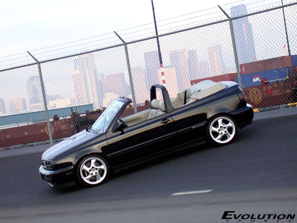 Black convertible with tan interior parked on an incline, viewed from the front-right