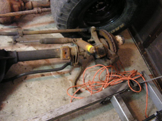 Front axle assembly with shock absorber, brake rotor, and suspension parts. Orange cord is coiled nearby