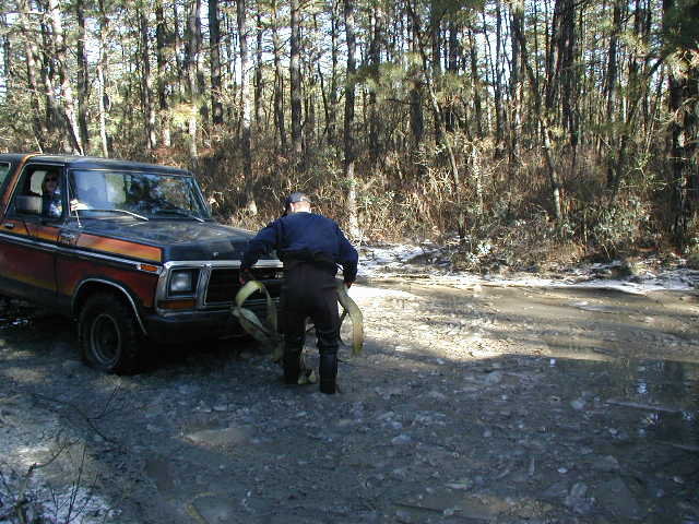 Person hooking a tow strap to a black flamed Ford truck on a muddy winter trail