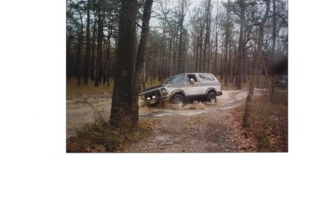 1979 Ford Bronco - A two-tone Ford Bronco navigates a water-filled path in a forest setting.
