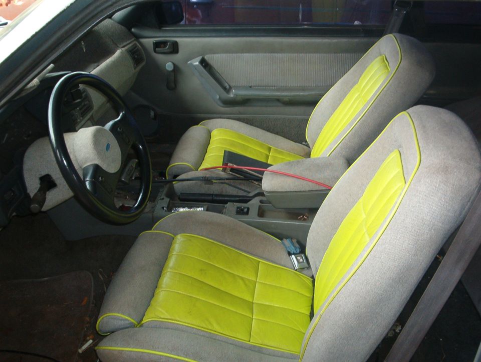 Front bucket seats reupholstered in gray and yellow inside a Ford coupe, console exposed