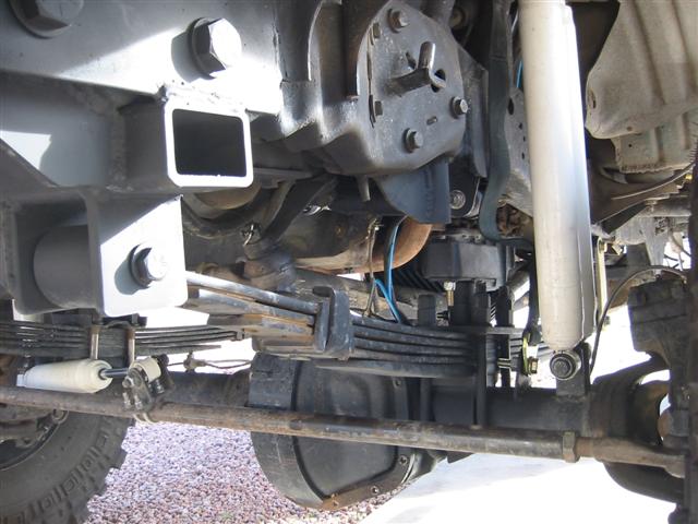 Underbody view of a lifted 4x4 front solid axle with leaf springs, white shocks, and steering stabilizer