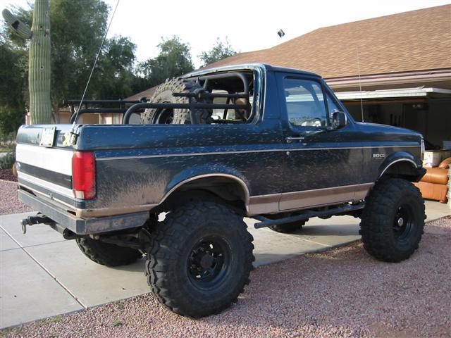 Lifted blue and tan topless Ford Bronco with roll cage parked on a desert driveway