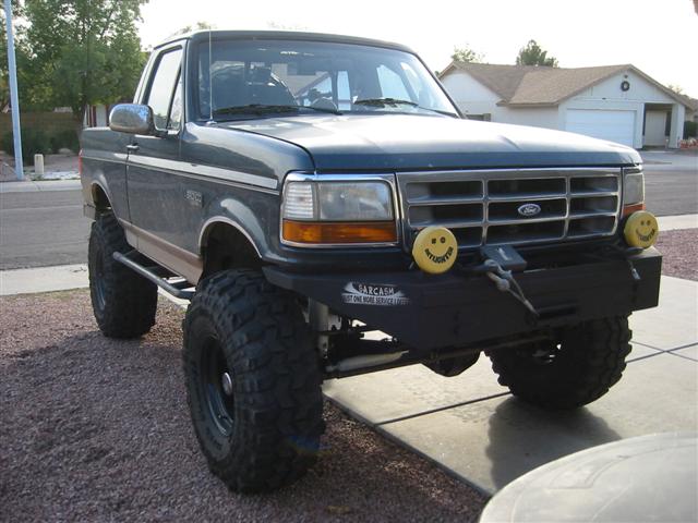 Lifted green Ford Bronco on mud tires with smiley bumper lights in a driveway