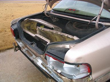 1999 Ford Crown Victoria - The rear of a tan sedan is shown with its trunk open, revealing spare tire and bumper components.