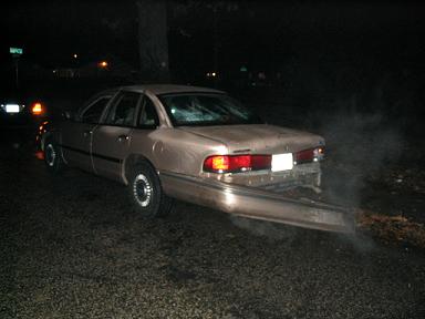 1999 Ford Crown Victoria - This sedan has significant rear-end damage, with the bumper hanging off and smoke emitting from the undercarriage.