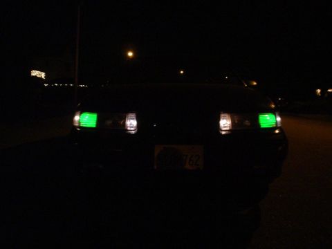 1993 Ford Taurus - A dark sedan with unusual green headlights is parked at night.